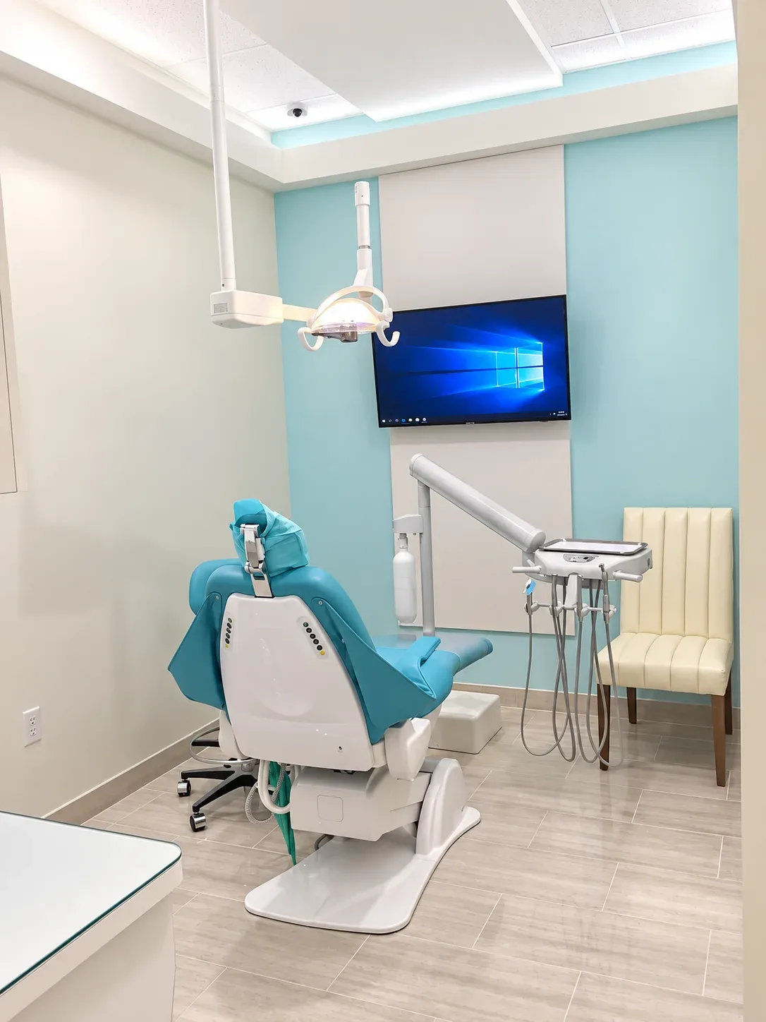 Treatment room with teal dental chair, overhead light and wall monitor