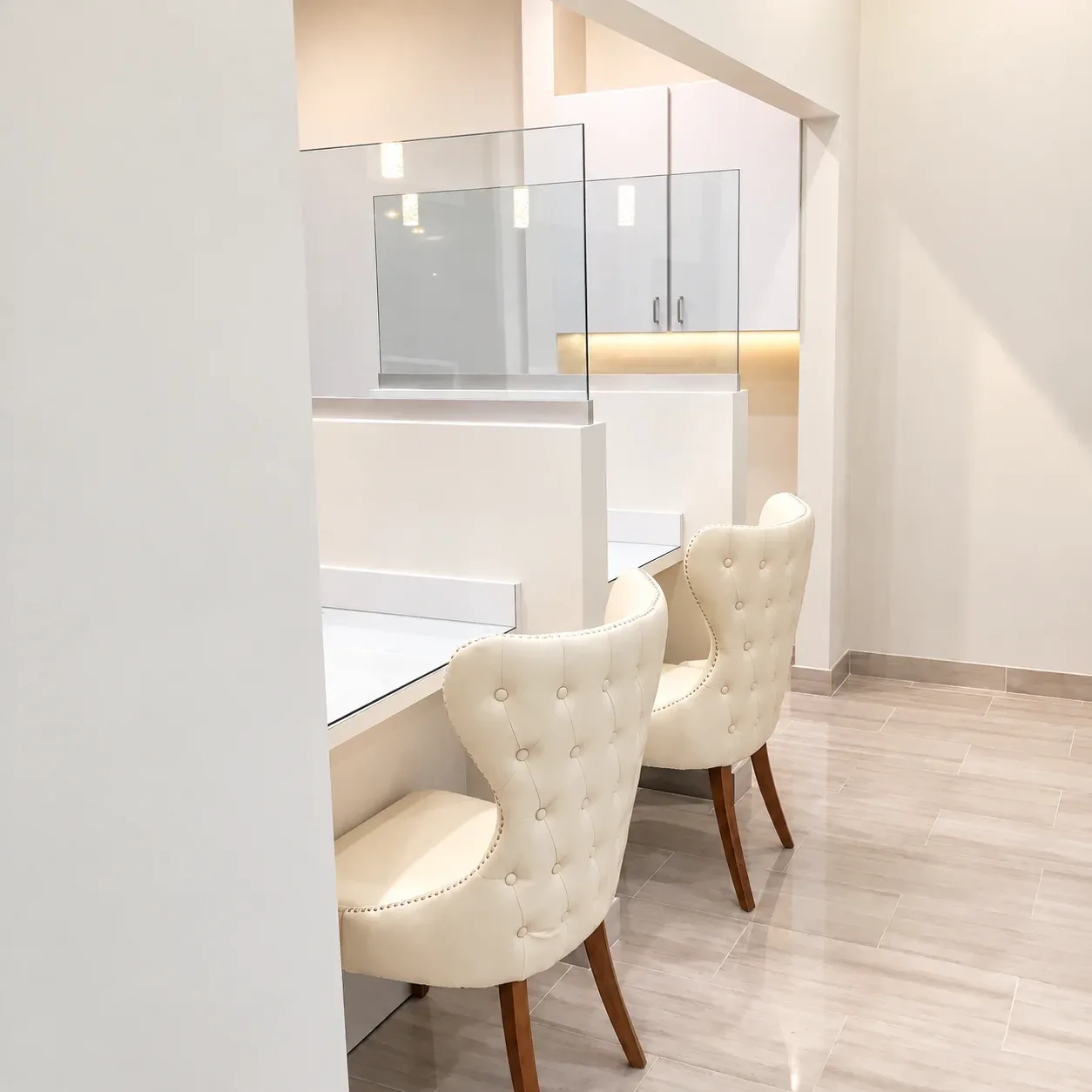 Cream tufted chairs at white counters with glass dividers